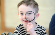 boy holding up a magnifying glass and looking at the camera